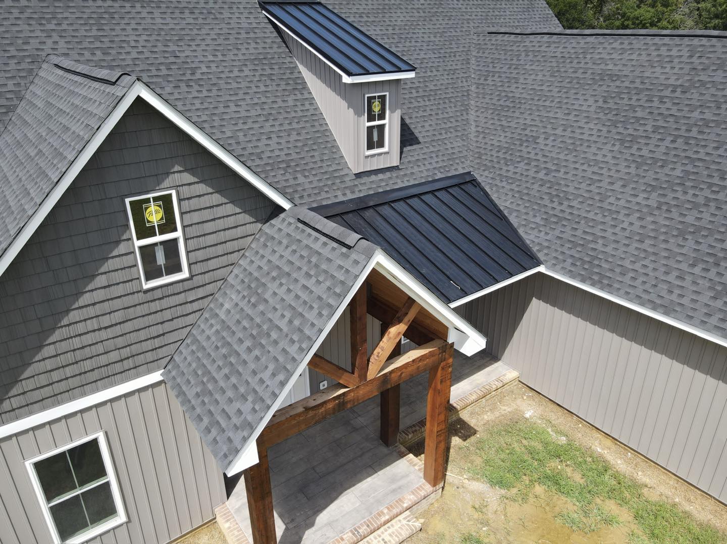 Aerial view of a gray house roof with blue solar panels and a wooden porch entry