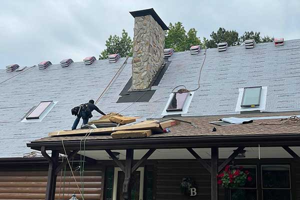 Worker kneeling on scaffolding, installing slate roof near chimney and skylights