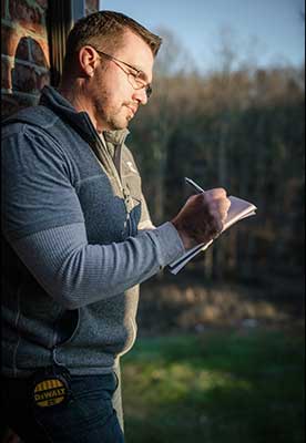 Man in glasses writing in a notebook outdoors in sunlight