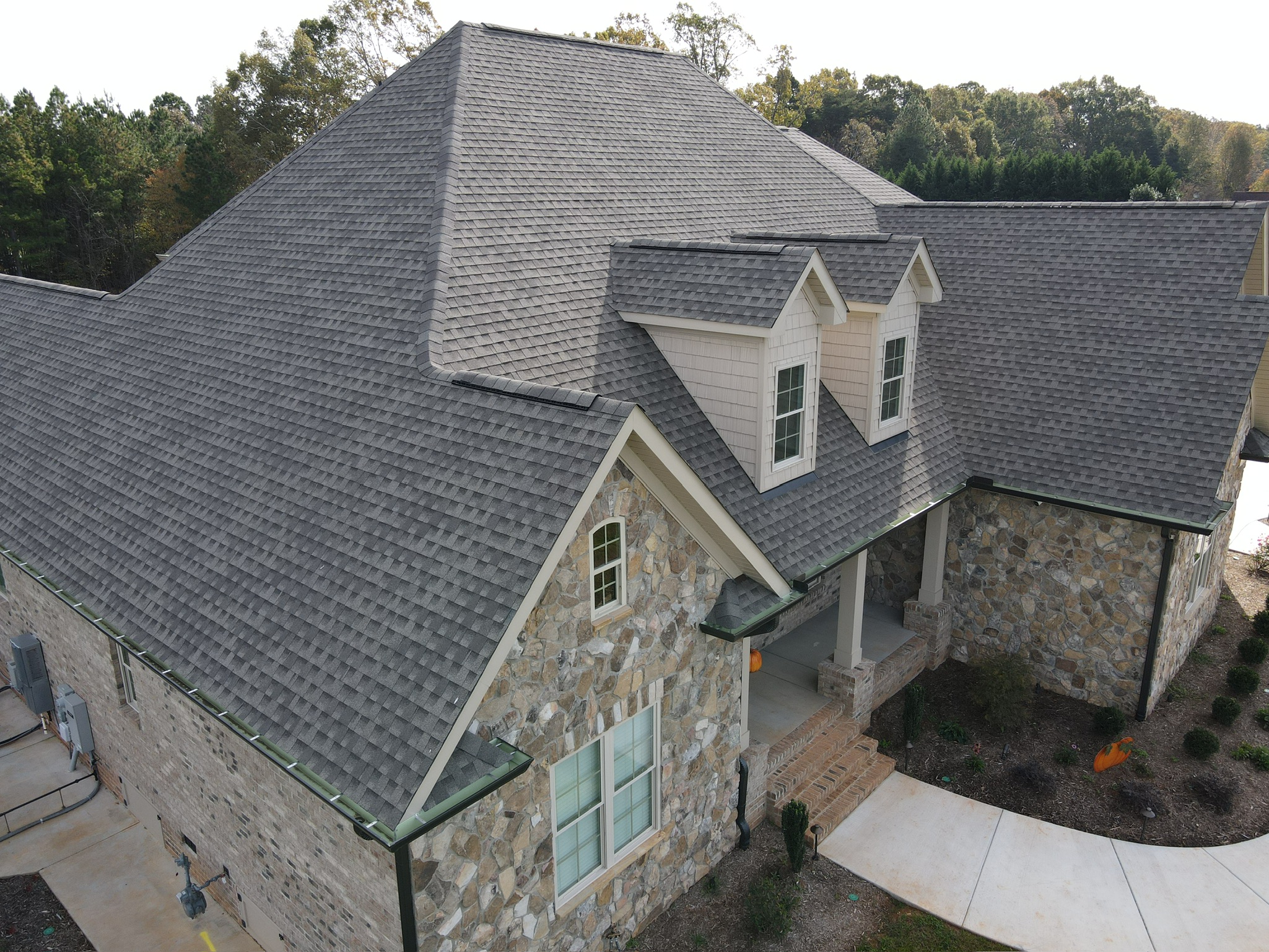 Aerial view of a large stone house with a gray shingle roof and dormer windows.