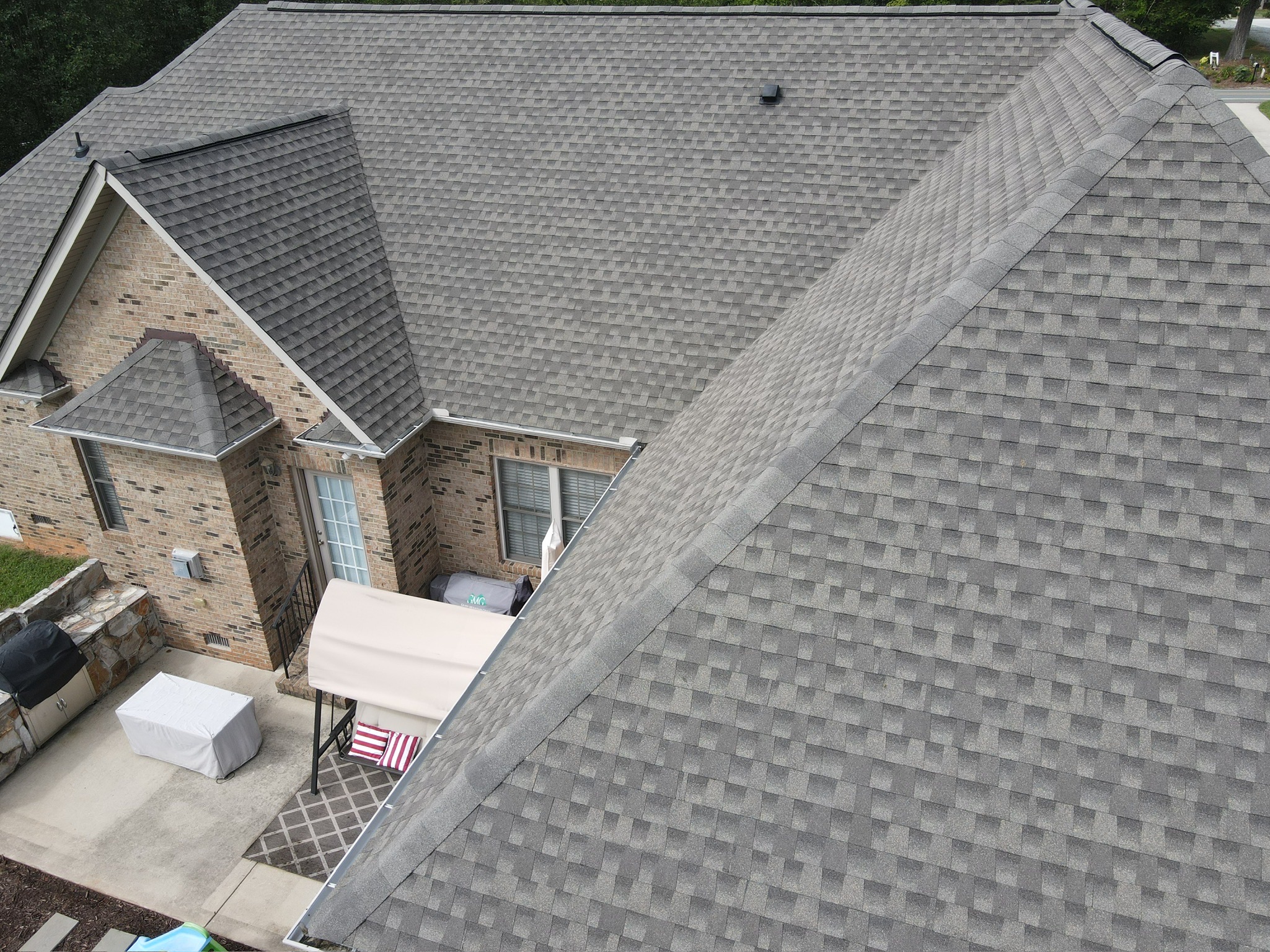 Aerial view of a gray-shingled house roof with dormer and patio.