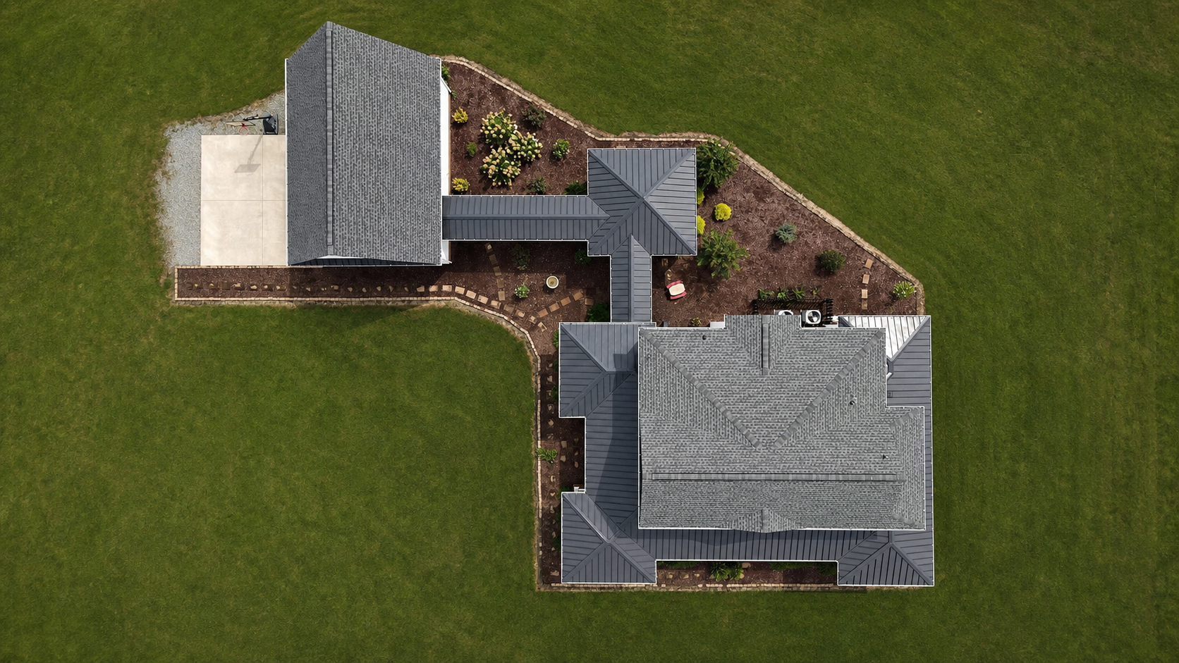 Aerial view of a gray-roofed house and landscaped yard surrounded by lawn